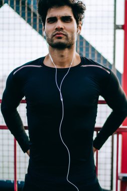 Ciddi motive genç atletik erkek portresi müzik dinleme ve egzersiz tanding kentsel ortamda hazırlama siyah eşofman giymiş. Modern kulaklık aktif giyim giymiş sporcu