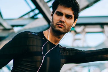 Profesyonel sporcu ısınma ve şişe modern kulaklık müzik dinleme sırasında elinde tutan eşofman giymiş. Kentsel ortamda spor egzersizleri yapıyor etkin aşınmaya motive fit adam