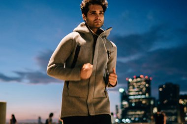 Motive erkek koşucu kentsel ayarlama ve kulaklık Müzik çalarda akşam egzersiz sırasında dinleme çalıştıran gri eşofman giymiş. Sporcu aktif giyim, açık havada alacakaranlıkta eğitim