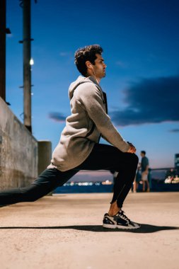 Profesyonel spor eğitim akşam saat sırasında ayak üzerinde germe egzersizleri yapıyor adam uygun. Kentsel ortamda egzersiz daha iyi sağlıklı canlılık için önce ısınma genç atlet yan görünüm