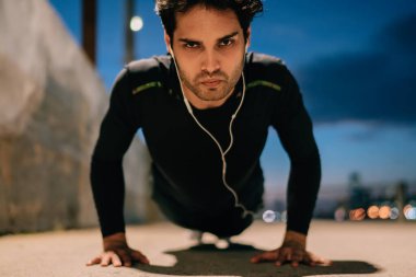 Kulaklık müzik dinleme ve alacakaranlıkta yere kadar iterek etkin aşınmaya motive fit adam portresi. Canlılık korumak için ciddi sporcu akşam egzersiz sırasında spor egzersizleri yapıyor