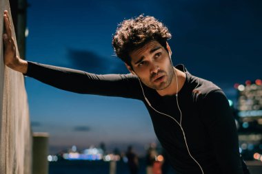 Yorgun uygun adam tatilinde zor akşam egzersiz sonrasında duvara yaslanmış kulaklık ses müzik dinleme eşofman giymiş. Etkin aşınmaya erkek koşucu spor eğitim açık sonra bitkin