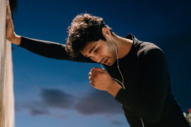 Delikanlı sevgilisi sporun kentsel ayarlarında çalıştığını akşam sonra duvara yaslanmış yorgun. Eşofman dinleme müzik kulaklık modern şehir içinde çalışmadan sonra mola sırasında yorgun erkek atlet