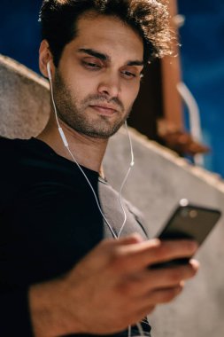 Erkek koşucu görünümü altında spor eğitim ayakta kentsel ortamda akşam için müzik uygulama seçme spor elbise giymiş. Modern kulaklık için egzersiz açık havada ses dinleme Runner