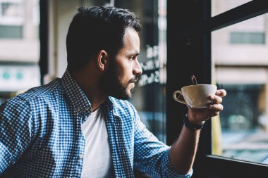 Dalgın sakallı hippi adam zevk sabah kahve kahvaltı away kafeterya penceresinde aramak için rahat kıyafet sırasında içecek içme düşünceli beyaz erkek kırmak kafede iç