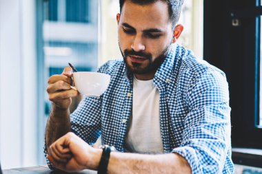 Genç beyaz erkek bu kol saati netbook, dizüstü bilgisayar bilgisayar yazılımı güncelleştirmek için bekleyen zaman holding Kupası kontrol öğrenci ile office coworking oturmuş kahve molası sırasında seyir geliştirici