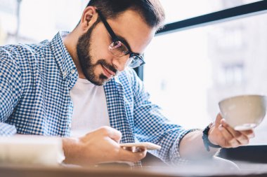 Dalgın hipster adam üzerinden mobil kafe, genç erkek blogger yükleme içerik ağlarında smartphone içme kahve üzerinden takipçileri ile paylaşımı oturan uygulama yapma işlem konsantre