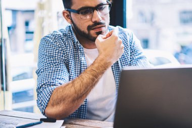 Konsantre hipster adam dizüstü bilgisayar üzerinde online kurslar uzak iş yapıyor kafe iç, düşünceli grafik tasarımcı proje bilgisi çözümlenirken içinde otururken eğitim öğretici izliyor