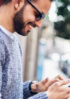 Komik resimler şehir sokak üzerinde duran smartphone üzerinden ağ ile ilgilenen hipster adam gülümsüyor, neşeli genç adam cep telefonu açık havada üzerinde rezervasyon uygulaması ile memnun kazanmaktan memnun