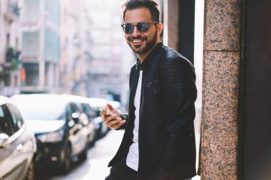 Sosyal ağlar, şehir sokak bloglama mutlu yakışıklı erkek arkadaş online telefon aracılığıyla kamera sohbet seyir üzerinde smartphone ayakta kullanarak neşeli hipster adam portresi yarım uzunluk