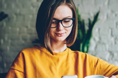 Sosyal ağ profili güncelleştirme ve smartphone kablosuz 4 g internet keyfi lezzetli kahve için boş zamanlarında bağlı Web sitesi içinde iş yazı yayınlama gözlük içinde büyüleyici kadın blogger