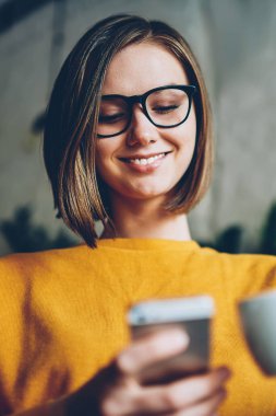 Şık saç kesimi ve süre komik fotoğraf uygulama yükleme ve smartphone ücretsiz Wi-Fi bağlantısıyla Cafe takipçileri ile mesajlaşma kapuçino keyfi gözlük ile pozitif kadın internet kullanıcı