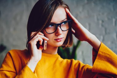 Gözlüklü ciddi bir iş kadınının görüş düzeltmesi için düşünmesi akıllı telefon cihazını ararken başka yöne bakması ve sorunu çözmekten bahsetmesi. Telefonla iletişim kuran kendinden emin genç bir kadın.