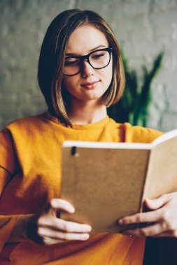 Şık kısa saç kesimi ve sahte markası kafede dinlenme alanı ile ilginç kitap okuma gözlük olan akıllı kadın. Zeki kadın harcama zaman edebiyat bestseller üzerinde yoğunlaşmıştır.
