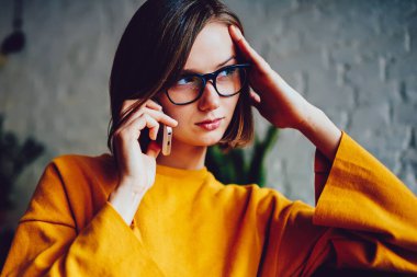 Gözlüklü ciddi bir iş kadınının görüş düzeltmesi için düşünmesi akıllı telefon cihazını ararken başka yöne bakması ve sorunu çözmekten bahsetmesi. Telefonla iletişim kuran kendinden emin genç bir kadın.