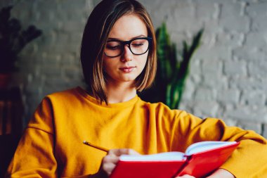 Görme düzeltmesi için gözlüklü dalgın hippi öğrenci kafeteryada oturup çizim yapıyor. Kafeteryada dinlenen defterine geleceğin planını yazan yaratıcı genç bir kadın.