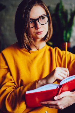 Kısa saç kesimi ve optik gözlükleri olan düşünceli genç bir kadın elinde not defteri tutarken gözlerini kaçırıyor ve kompozisyon yazmak için yaratıcı fikirler düşünüyor. Kitap okuyan hippi bir öğrenci.