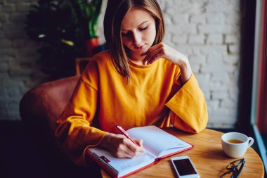 Düşünceli hippi kız not defterine boş vakitlerin tadını çıkararak kahve dükkanında masaya oturmuş kontrol listesi yazıyor. Not defterine makale yazan genç bir kadın kafede ders çalışmaya hazırlanıyor.