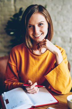 Yarım uzunluk ile şık kısa saç kesimi sabah zaman içinde kahve, Not defterinizdeki notlar verme kamera gülümseyen güzel neşeli öğrenci portresi. Pozitif kadın sahibi çalışma planı yazma