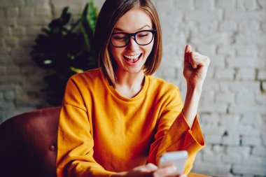 Kısa saçlı başarılı genç kadın akıllı telefondan canlı yayın izliyor ve favori takımın zaferini kutluyor. Çevrimiçi yarışmada kazanmaktan mutlu duygusal hippi kız.