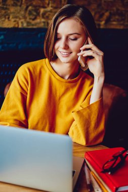 Modern dizüstü bilgisayarda kablosuz internet kullanarak akıllı telefondan arayan pozitif kadın serbest yazar. Yazılım güncelleme sırasında gülen ve konuşan neşeli genç kadın.