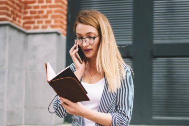 Teknoloji ve iletişim, profesyonel kadın gazeteci cep telefonuyla iletişim kurdu. Modern akıllı telefondan konuşan genç, ciddi bir hippi kız açık havada defter tutuyor.