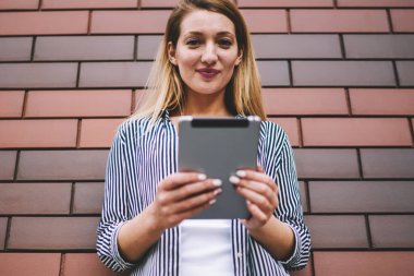 Sosyal ağdaki takipçilerle sohbet etmek için modern taşınabilir bilgisayar kullanan, reklam metni ve mesajları için fotokopi alanının yakınında duran ve kameraya bakan pozitif kadın blogcu