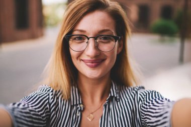 Yüzünde tebessüm olan çekici hippi kızın selfie portresini kapat şık gözlükleriyle şehirde boş zamanların tadını çıkar, kameraya bakan ve dışarıda bekleyen son moda kadının.