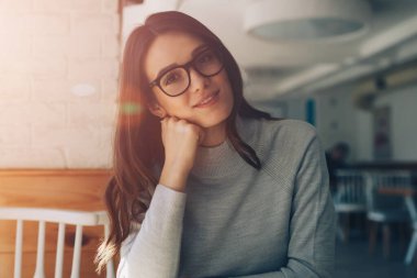 Güneşli bir günde evde oturup eğlenen gülümseyen genç kız portresi, kafeteryada dinlenip ara verdiğimizde kameraya bakan gözlüklü mutlu kadın.