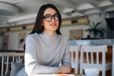 Kafeteryada öğrenim gören, gözlerini kaçırıp gülümseyen, mutlu blogcu, kafeteryada keyif çatan, şık gözlüklü, kapalı alanda fikir üzerinde kafa yoran pozitif bir kadın.