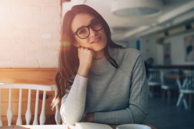 Güneşli bir günde evde oturup eğlenen gülümseyen genç kız portresi, kafeteryada dinlenip ara verdiğimizde kameraya bakan gözlüklü mutlu kadın.