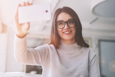 Cep telefonu kamerasına bakıp kendini gösteren mutlu kadın blogcu, kafeteryada oturan başarılı hippi kız ve selfie çekmek için akıllı telefonu kullanıyor.