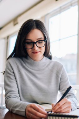Kafeteryada çalışan zeki bir kız öğrenci bilgi aramak için netbook kullanıyor, kafeterya hakkında yazı yazmak için moda gözlüklü çekici yaratıcı hippi kız.