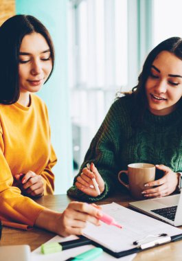 Dizüstü bilgisayar aygıtla masaüstü stüdyoda oturan gelişmekte olan başlangıç projesi için iş planı kontrol iş kadınları. İki öğrenci üniversitede banka görev üzerinde beyin fırtınası sırasında işbirliği