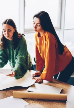 Üç kadın tasarımcılar skeçler Office birlikte çalışma rahat kıyafet giymiş. Dalgın genç profesyonel Mimarlar proje ayakta masaüstü planları Studio ile bina çalışma