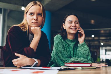 Sinir bozucu sarışın genç kadın sorunları üzerinde düşünme ve uzak smartphone aygıt birlikte kitap ile masaüstünde oturan telefon görüşme sırasında gülüyor neşeli en iyi arkadaşı iken arıyorsunuz