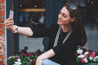 Pozitif kız öğrenci şehir ortamında zaman harcıyor ve kendi internet günlüğü için selfie çekiyor ön kamerayı açık havada kullanıyor, modaya uygun giyinmiş başarılı hippi kız açık havada fotoğraf çekiyor.