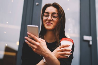 Genç olumlu çekici kadın sohbet ve takipçileri cep kullanarak sosyal ağlar ile haber paylaşımı ve Internet bağlantısı. Mutlu genç serbest zaman açık havada gadget ve kahve keyfini