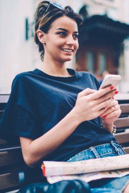 Başarılı kadın turist, yeni modern akıllı telefonları kullanarak uluslararası hafta sonu geçirmekten mutlu. Gezici, pozitif, kaygısız hippi kız, elinde cep telefonuyla diğer tarafa bakıyor.