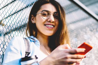 Gözlük bloglama sosyal ağlar açık havada serbest zaman sahip kız öğrenci gülümseyen, neşeli genç kadın manifatura mesaj mobil arkadaşlarınızla sohbet üzerinde sokakta duran tarifeler ile memnun
