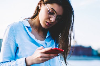 Dalgın hippi kız Eyewear Kahve kaldı Nehri yakınında, düşünceli kadın blogger yükleme fotoğrafları ile ağ okuma geri bildirimler için takipçileri dinlenme smartphone web sayfasında haber okuma