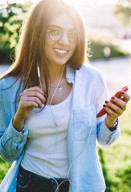 Güneşli bir günde parkta dinlenirken akıllı telefondan SMS gönderen, gülümseyen hippi kız portresi, kulaklıkla müzik dinlemekten hoşlanan, telefonla şarkı seçen, gündelik giyinen genç bir kadın.