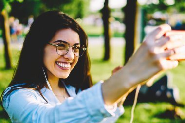 Mutlu kız öğrenci selfie smartphone kameraya yapmak için poz rekreasyon ile paylaşım ağlarında için güneşli Park dinlenme sırasında resim yolu ile hareket eden alarak neşeli hippi kız memnun.