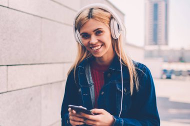 Yarım uzunluğu playlist ayakta kentsel ortamda gözde şarkı seçerken kameraya gülümseyen mutlu genç kadın portresi. Neşeli öğrenci dinleme ses kaseti yürüyüş sırasında modern Kulaklığımda