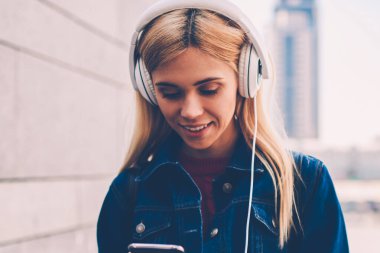 Hippi kız Kot ceket smartphone cep telefonu ile kentsel bir ortamda yürüyüş modern Kulaklığımda dinleme ses şarkı süre gelen bildirim okuma gülümseyerek. Neşeli öğrenci telefonda Sohbet Online