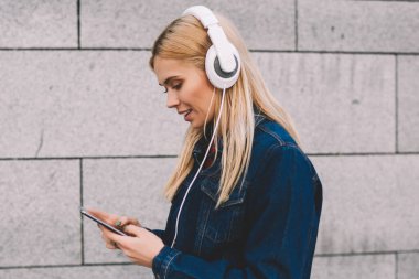 Hippi kız kot giyim gri promosyon arka plan yürüyüş modern Kulaklığımda dinlemek için smartphone cep telefonu ile müzik uygulamasında ses şarkı seçme giymiş yan görünüm
