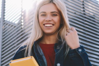 Muhteşem olumlu kız öğrencinin yarım uzunluk portre güneşli kentsel ayarda geziniyor trendy denim giyim giymiş. Şirin neşeli hippi kız kameraya Street yaz yürüyüş sırasında