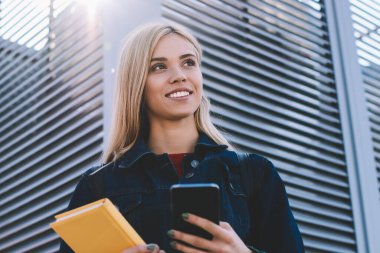 Genç kadın blogger gülümseyen sevimli uzak bilgisayar yazılımı üstünde cep telefonu açık havada güncelleştirilirken seyir trendy kıyafetler giymiş. Aygıt ile güneşli Street ücretsiz vakit şirin olumlu hippi kız