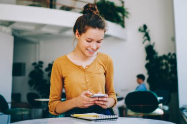 Neşeli gülümseyen kadın blogcu sosyal ağlarda kendi içeriğini ararken aynı zamanda modern akıllı telefon, teknoloji ve iletişim konsepti üzerinden arkadaşından gelen olumlu mesajı okuyor.