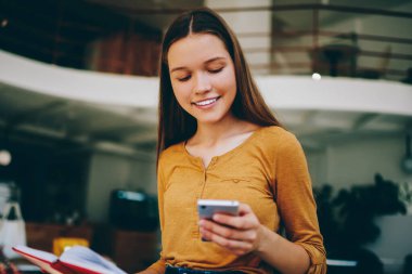 Mutlu gülümseyen hippi kız takipçilerle sosyal ağlarda sohbet etmek için başvuruda bulunuyor, olumlu kadın bildirimi kontrol ediyor ve cep telefonu ve edebiyat ile boş zamanların keyfini çıkarıyor